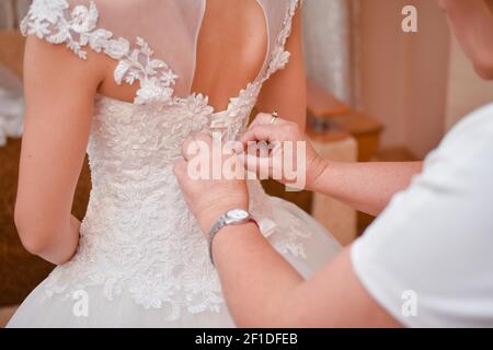 La madre della sposa aiuta la sposa a vestirsi. Foto Stock