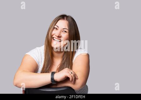 Giovane bella donna dai capelli lunghi con trucco naturale su sfondo grigio Plus taglia modello sorridente cute guardando in lontananza. Ritratto di un felice e. Foto Stock