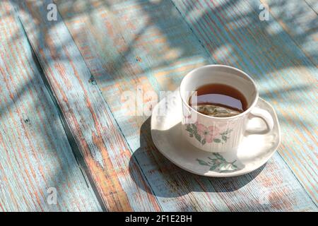 Tazza di tè su tavolo rustico in legno con ombra di foglie di palma. Foto Stock