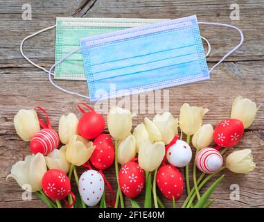 Festa di Pasqua a Coronavirus pandemia. Maschere di protezione Covid19, uova di Pasqua e tulipani su sfondo di tavola di legno Foto Stock