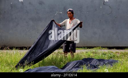 Lavoratori che asciugano il panno batik in campo, in una giornata calda, Pekalongan, Indonesia, 8 marzo 2021 Foto Stock