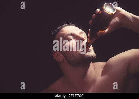 Un ragazzo muscoloso di stile gode del gusto della birra artigianale. Foto di studio su sfondo scuro Foto Stock