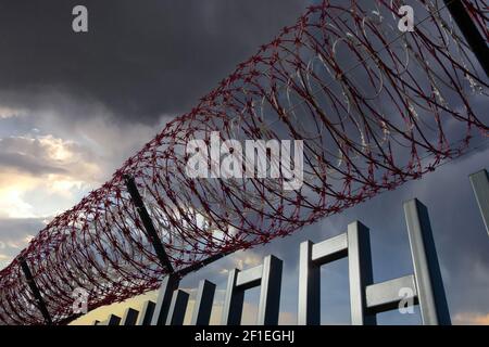 Bobina di filo spinato come barricata contro il Trespasser su un cielo cupo nuvoloso. Foto Stock