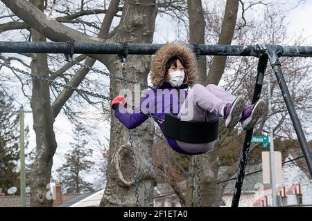 Un adolescente americano asiatico mascherato si allena su un'altalena a Kissena Park, Flushing, New York Foto Stock