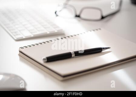 primo piano del blocco note a spirale con penna a sfera sulla scrivania da ufficio bianca, prendendo appunti Foto Stock
