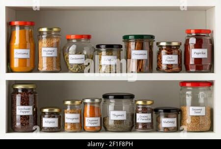Vasetti di vetro riciclati con una varietà di erbe essiccate in una fila sul ripiano della cucina Foto Stock