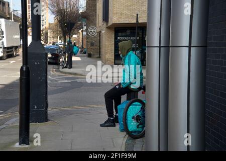 Londra, Mare Street, Hackney, Regno Unito. Deliveroo Cyclist in attesa di consegna Foto Stock