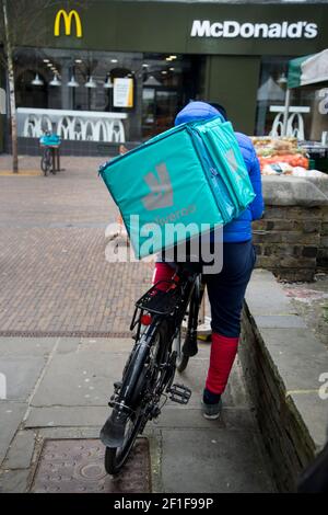 Londra, Hackney, Regno Unito. Deliveroo ciclista in attesa di ritirare la consegna da McDonalds. Foto Stock