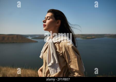 Bella donna dai capelli scuri in abito casual godendo di incredibile natura al parco nazionale Podillya Tovtry. Donna turistica in piedi su yop di montagna con occhi chiusi. Foto Stock