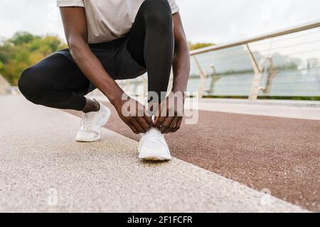 Sportivo afroamericano che lega i suoi lacci per scarpe mentre si allenano su un ponte urbano all'aperto Foto Stock