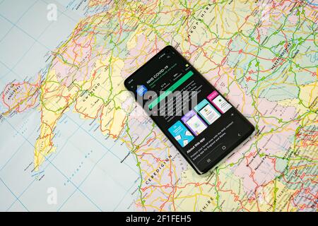 Smartphone con app NHS COVID-19, app National Health Service, visualizzata su Google Play con mappa del Regno Unito e maschera facciale sullo sfondo Foto Stock