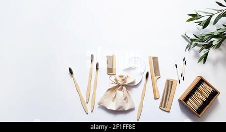 Spazzolini da denti in bambù organico, bastoncini per le orecchie e spugne di cotone riutilizzabili su sfondo bianco con interessanti ombre di rami d'oliva. Zero sprechi essenziali Foto Stock