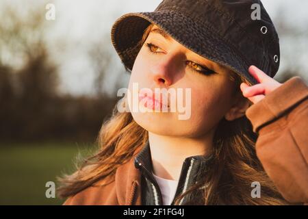 bel primo piano ritratto di una bella ragazza adolescente faccia nell'ora d'oro del sole che fissa un grande cappello floppy Foto Stock