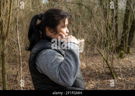 Una donna asiatica di mezza età in una foresta primaverile. Alberi e cespugli sullo sfondo Foto Stock