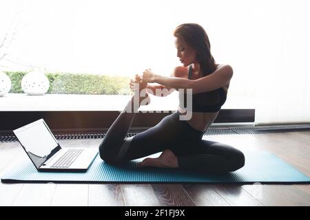 Giovane donna che fa esercizio stretching a casa sulla base di tutorial, e-learning Foto Stock