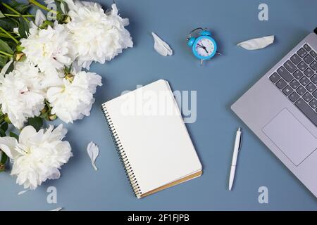 apri il notebook per scrivere piani, per fare lista o sogni con peonie fresche, computer portatile, sveglia, su sfondo azzurro Foto Stock