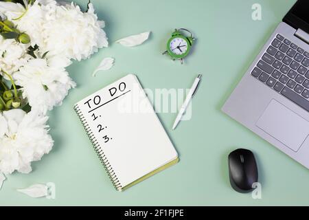 apri il notebook per scrivere piani, per fare lista o sogni con peonie fresche, computer portatile, sveglia, su sfondo verde chiaro Foto Stock