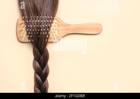 Spazzola per capelli con treccia di capelli marrone femmina su sfondo beige. Hairdresser concetto di salone e acconciature Foto Stock