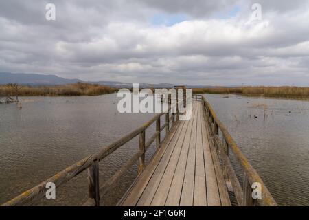 Un lungo molo in legno e una passerella in zone umide di acque salmastre con erba esparta e laguna sotto un cielo sovrastato Foto Stock