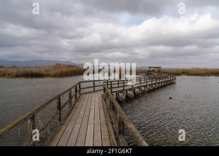 Un lungo molo in legno e una passerella in zone umide di acque salmastre con erba esparta e laguna sotto un cielo sovrastato Foto Stock