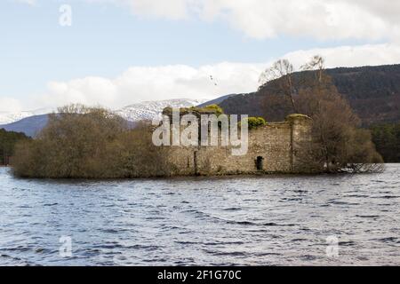 La rovina di un piccolo castello su un'isola di Loch An Eilein, parte della tenuta Rothiemurchus ad Aviemore, Scozia, con montagne innevate nella ba Foto Stock