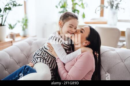 Madre con piccola figlia seduta sul divano all'interno di casa, baciando. Foto Stock