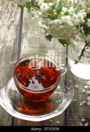 Tè floreale di primavera del biancospino con rami fioriti di primavera con boccioli di fiori su sfondo di legno, concentrarsi sul riflesso di fiori nel tè, closeup, c. Foto Stock