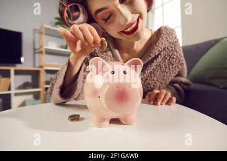 Felice giovane donna che fa piani per il futuro e mettere monete nella sua banca piggy Foto Stock