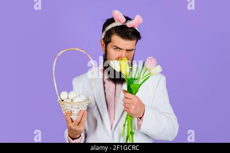 Giorno di Pasqua. Uomo con bouquet di tulipani con uova a cesto. Bel maschio con orecchie conigliate. Foto Stock