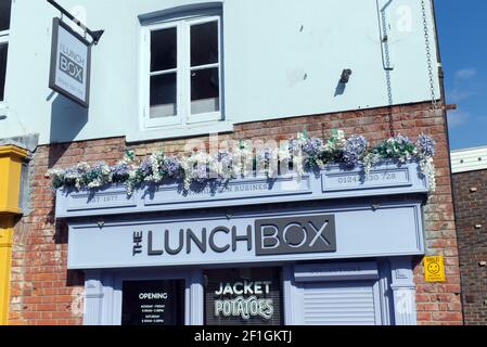 Il Lunch Box Cafe per deliziosi panini e torte a Chichester con una mostra di fiori sopra il cartello del cafe'. Foto Stock