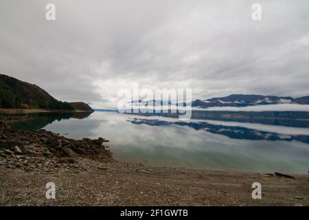 Lago Hawea, Isola del Sud della Nuova Zelanda. Vista incontaminata attraverso l'acqua blu che riflette le nuvole e la nebbia di montagna Foto Stock