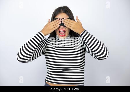 Giovane bella bruna bruna donna bruno indossare maschera che copre gli occhi con le mani sorridenti allegro e divertente. Concetto cieco. Foto Stock