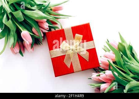 Confezione regalo rossa con arco dorato e bei tulipani su sfondo bianco, vista dall'alto Foto Stock