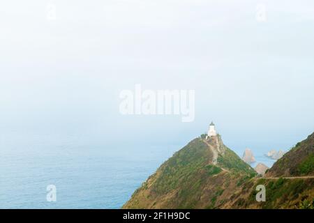 Faro di Nugget Point sulla costa selvaggia e nebbiosa dell'Oceano Pacifico, l'orizzonte scompare in bianco nebbia astratta, un famoso punto di riferimento a sfondo di nebbia bianca Foto Stock