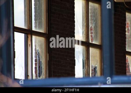 Vista interna di un vecchio, scentrante, e abbandonato edificio di fabbrica. Grande camera vuota con pareti in mattoni, travi a vista e lampade a luce fluorescente. Foto Stock