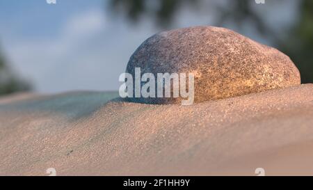 Pietra sulla spiaggia al tramonto con il cielo e gli alberi in background 3d illustrazione Foto Stock