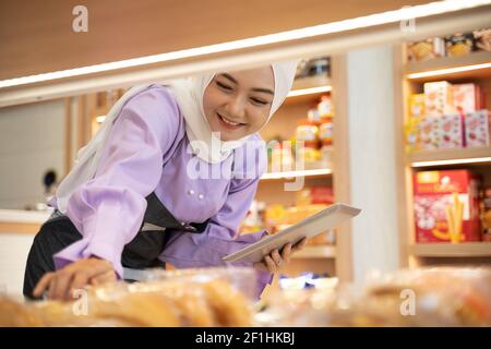 proprietario musulmano di affari che controlla il suo prodotto sul display dentro il negozio Foto Stock