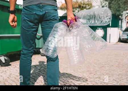 Uomo gettando fuori vuoto usato grandi bottiglie d'acqua di plastica nel contenitore principale dei rifiuti. Bottiglie d'acqua non riciclabili. Problemi di acqua in bottiglia e inquinamento Foto Stock