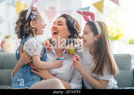 Buona vacanza! Madre e le sue figlie con uova di pittura. La famiglia festeggia la Pasqua. Le ragazze piccole cute dei bambini stanno portando le orecchie del coniglietto. Foto Stock