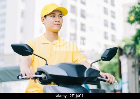 La persona asiatica di consegna sta guidando la sua motocicletta per trasportare a. cliente Foto Stock
