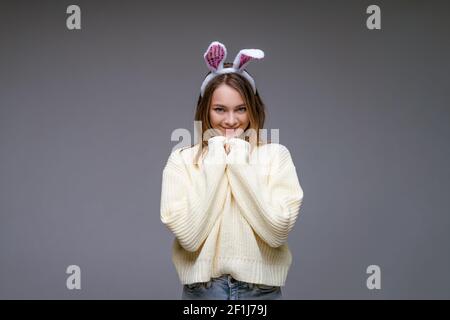 giovane donna, bionda, con orecchie bianche e un maglione leggero su sfondo grigio Foto Stock