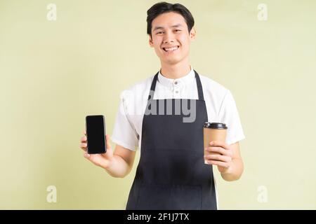 Cameriera asiatica che tiene un telefono e una tazza di carta dentro una mano sorride Foto Stock