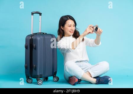 Bella donna asiatica seduta in posa accanto a valigia e di preparazione per viaggi Foto Stock