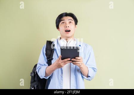 Studente asiatico maschile che stava usando il tablet e guardato con un'espressione sorpresa Foto Stock