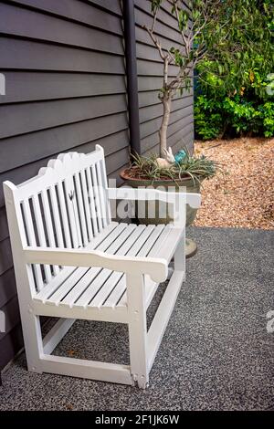 Una sedia di legno bianco accanto a una pentola decorativa pianta in un giardino Foto Stock