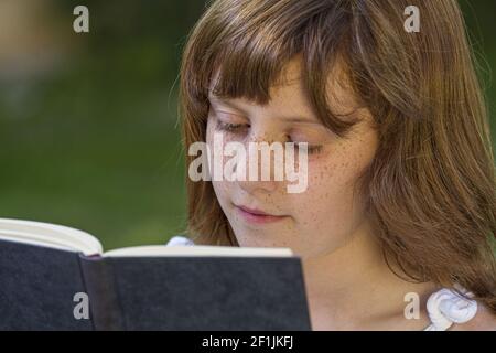 Ragazza rossa che legge un libro in un parco con bella erba verde, natura e vita sana Foto Stock