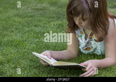 Imparare, ragazza rossa leggere un libro in un parco con bella erba verde, la natura e la vita sana Foto Stock