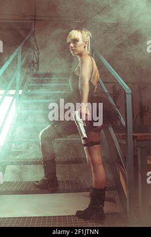 Ragazza bionda con pistole in una fabbrica abbandonata. cosplayer, azione e pericolosa donna Foto Stock