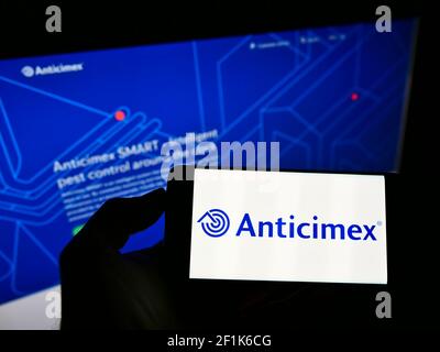 Persona che tiene il cellulare con il logo della società svedese di controllo dei parassiti Anticimex AB sullo schermo di fronte alla pagina web aziendale. Mettere a fuoco il display del telefono. Foto Stock