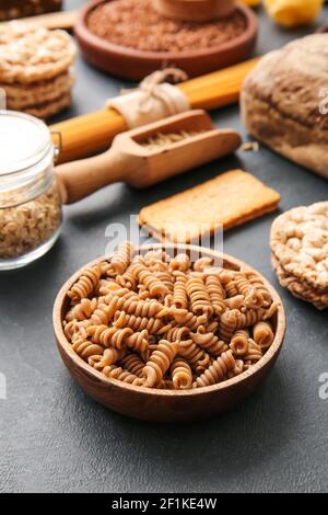 Ciotola con pasta cruda e prodotti diversi su fondo scuro, primo piano Foto Stock